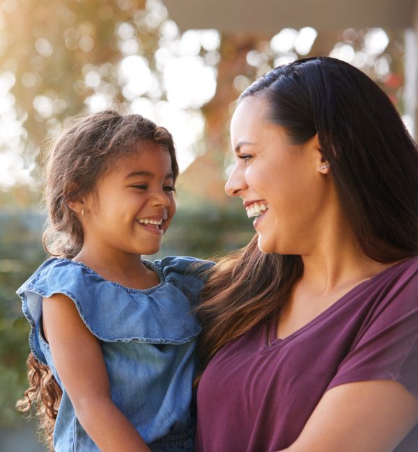 Smiling Hispanic Mother Holding Daughter Laughing In Garden At Home